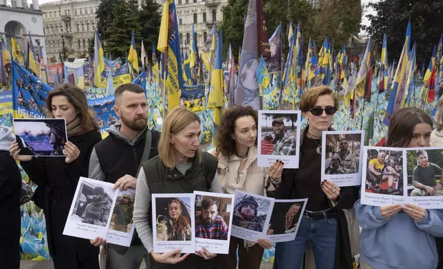 People hold photos of their relatives soldiers to keep a nationwide minute of silence in memory of fallen soldiers, who defended their homeland in war with Russia, on Defenders Day at the improvised war memorial in Independence square in Kyiv, Ukraine, Tuesday, Oct. 1, 2024. (AP Photo/Efrem Lukatsky)