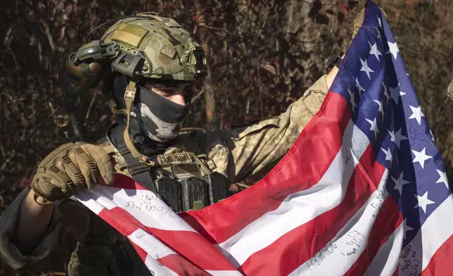 FILE - A 25-year-old volunteer fighter identified only as Dima, who is from the U.S. state of Texas and serves with the 23rd rifle battalion of Ukraine’s armed forces, holds a U.S. flag near the front line in the Kharkiv region of Ukraine, on Oct. 26, 2024. (AP Photo/Efrem Lukatsky, File)