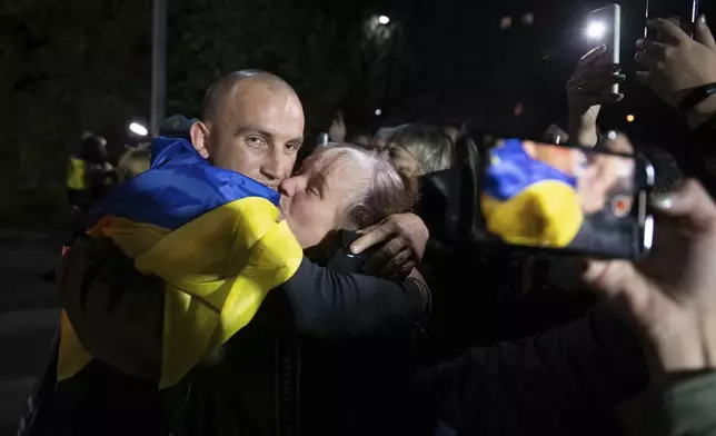 In this photo provided by the Press Service of the President of Ukraine on Oct. 19, 2024, a Ukrainian serviceman with National flag hugs his relative after returning from captivity during a POWs exchange in an undisclosed location, Ukraine. (Press Service of the President of Ukraine via AP)