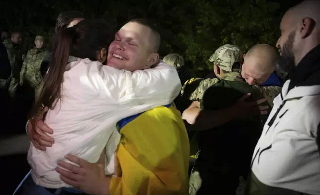 In this photo provided by the Press Service of the President of Ukraine on Oct. 19, 2024, a Ukrainian serviceman covered with a national flag hugs his relative after returning from captivity during a POWs exchange in an undisclosed location, Ukraine. (Press Service of the President of Ukraine via AP)