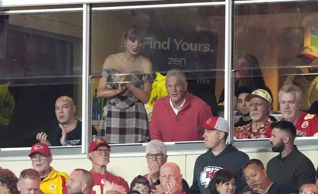 Taylor Swift stands as she watches from a suite next to her dad Scott Swift during the first half of an NFL football game between the Kansas City Chiefs and the New Orleans Saints Monday, Oct. 7, 2024, in Kansas City, Mo. (AP Photo/Charlie Riedel)