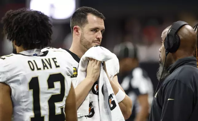 New Orleans Saints quarterback Derek Carr, center, speaks on the sidelines during the second half of an NFL football game against the Atlanta Falcons, Sunday, Sept. 29, 2024, in Atlanta. (AP Photo/Butch Dill)