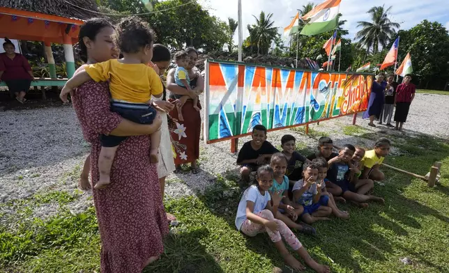 Women and children gather near a sign in a village near in Apia, Samoa, on Sunday, Oct. 20, 2024, that refers to their sponsored country of India ahead of the Commonwealth Heads of Government meetings starting later in the week. (AP Photo/Rick Rycroft)