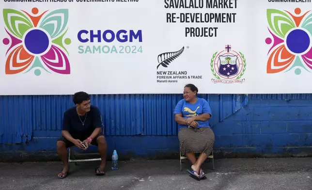 A man and woman rest in the shade of a Commonwealth Heads of Government banner in Apia, Samoa, on Monday, Oct. 21, 2024. (AP Photo/Rick Rycroft)