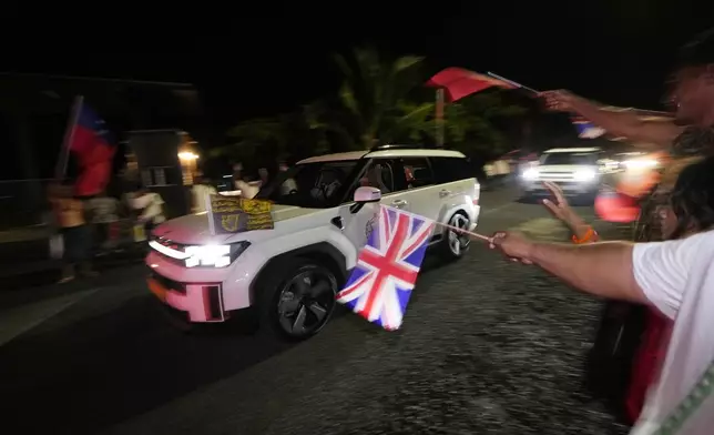 People wave flags as Britain's King Charles III and Queen Camilla arrive in the village of Siumu, Samoa, on Wednesday, Oct. 23, 2024. (AP Photo/Rick Rycroft)