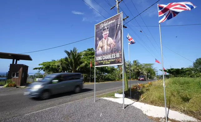 A car drives on a road decorated with flags and a portrait in the village of Siumu, Samoa, on Monday, Oct. 21, 2024, as the village prepares for the arrival of King Charles III. (AP Photo/Rick Rycroft)