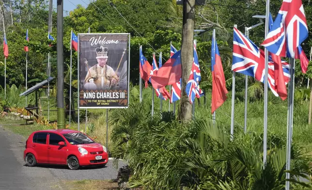 A car turns off a road decorated with flags and a portrait in the village of Siumu, Samoa, on Monday, Oct. 21, 2024, as the village prepares for the arrival of King Charles III. (AP Photo/Rick Rycroft)