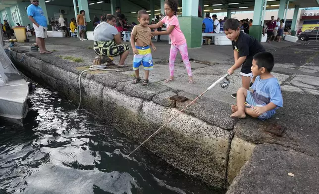 Children try their luck fishing off a dock next to a fish market in Apia, Samoa, on Sunday, Oct. 20, 2024. (AP Photo/Rick Rycroft)