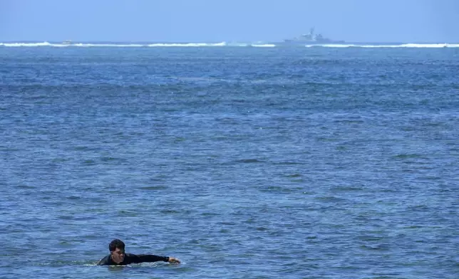 Michael Malae paddles into shore after surfing at Sima PJ Beach Fale resort in the village of Tafitoala, Samoa, on Monday, Oct. 21, 2024, near where a New Zealand navy ship ran aground and sank on Oct. 6. (AP Photo/Rick Rycroft)