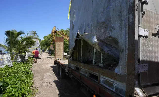 An excavator is used to drag a shipping container onto the beach, left, as another sits on a trailer in the village of Mulivai Safata, Samoa, on Monday, Oct. 21, 2024, near where a New Zealand navy ship ran aground and sank on Oct. 6. (AP Photo/Rick Rycroft)