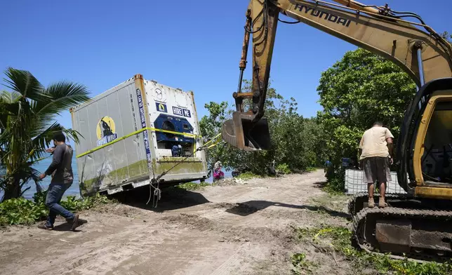 An excavator is used to drag a shipping container onto the beach in the village of Mulivai Safata, Samoa, on Monday, Oct. 21, 2024, near where a New Zealand navy ship ran aground and sank on Oct. 6. (AP Photo/Rick Rycroft)