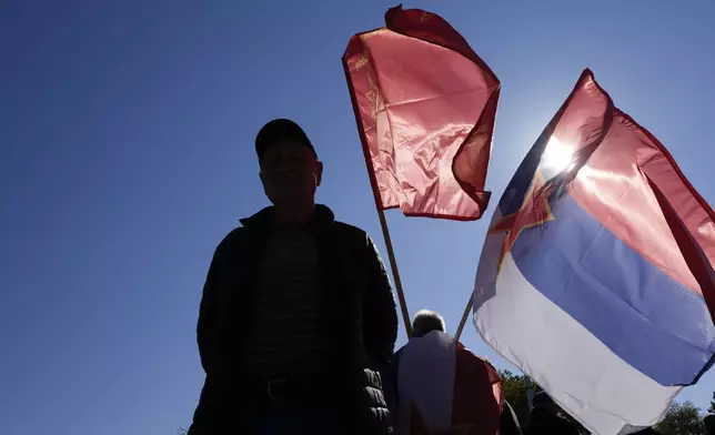 A man holds an old Yugoslav Communists' flag, top, and an old Serbian flag with the communist five-point star during the ceremony on the occasion of the 80th anniversary of the liberation of Belgrade from Nazi occupation in WWII by Soviet and local communist fighters, in Belgrade, Serbia, Sunday, Oct. 20, 2024. (AP Photo/Darko Vojinovic)