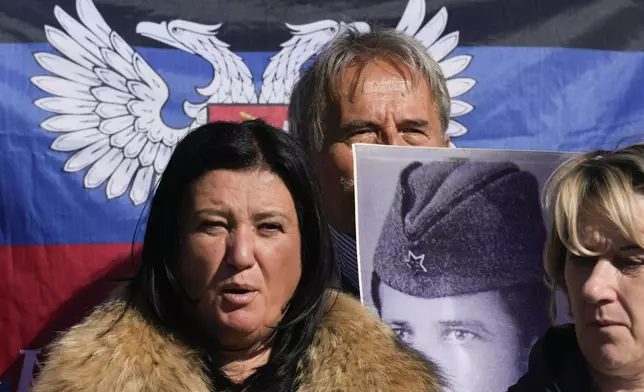 People hold a flag of the self-proclaimed Donetsk People's Republic and pictures of relatives killed in WWII during the ceremony on the occasion of the 80th anniversary of the liberation of Belgrade from Nazi occupation in WWII by Soviet and local communist fighters, in Belgrade, Serbia, Sunday, Oct. 20, 2024. (AP Photo/Darko Vojinovic)