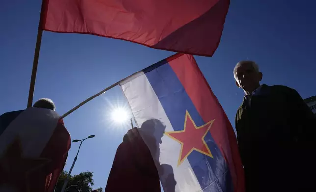 A man holds an old Yugoslav Communists' flag, top, and an old Serbian flag with the communist five-point star during a ceremony on the occasion of the 80th anniversary of the liberation of Belgrade from Nazi occupation in WWII by Soviet and local communist fighters, in Belgrade, Serbia, Sunday, Oct. 20, 2024. (AP Photo/Darko Vojinovic)