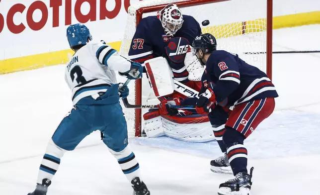 Winnipeg Jets goaltender Connor Hellebuyck (37) saves the shot from San Jose Sharks' Henry Thrun (3) as Dylan DeMelo (2) defends during the second period of an NHL hockey game, Friday, Oct. 18, 2024 in Winnipeg, Manitoba. (John Woods/The Canadian Press via AP)