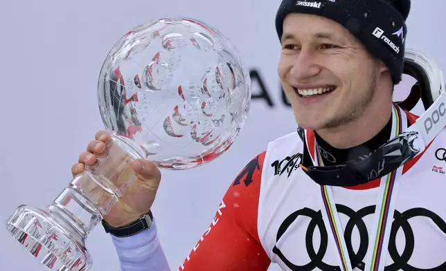 FILE - Switzerland's Marco Odermatt holds the alpine ski men's World Cup overall title trophy, as he celebrates on the podium, in Saalbach, Austria, on March 24, 2024. (AP Photo/Marco Trovati)