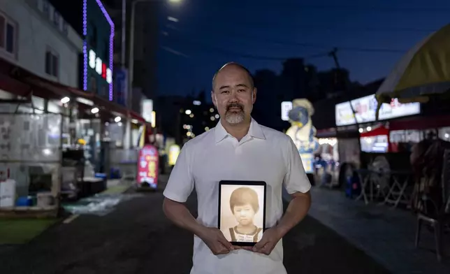 Kenneth Barthel, adopted from South Korea to Hawaii in 1979 at 6 years old, holds a tablet showing his childhood photo in Busan, South Korea, Thursday, May 16, 2024. Barthel is looking for his birth family in Busan where he believes he was abandoned when his mother ordered soup for him in a restaurant and never returned. (AP Photo/Jae C. Hong)