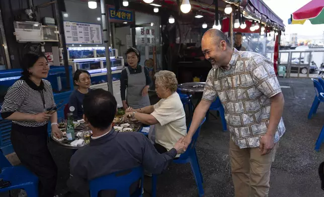 Kenneth Barthel, right, who was adopted to the United States at 6 years old, talks with diners in the neighborhood where he remembers being abandoned by his mother, in Busan, South Korea, Friday, May 17, 2024. Barthel was posting flyers in the area featuring his photos in the hopes of finding his birth family. (AP Photo/Jae C. Hong)