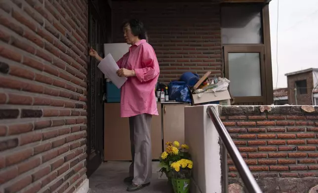 Holding a flyer asking for help to find adoptee Nicole Motta's birth family, long-time resident An Bok-rye knocks on the door of an apartment building where Motta's home once stood in Bucheon, South Korea, Thursday, May 30, 2024. Sympathetic residents, police officers and city workers of the towns where they once lived often try to assist adoptees searching for their origin story. (AP Photo/Jae C. Hong)