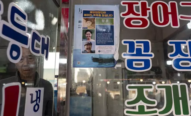 Restaurant owner Shin Byung-chul looks from behind a flyer he put up of Kenneth Barthel, who was abandoned in the area as a child and later adopted to Hawaii at 6 years old, at his restaurant in Busan, South Korea, Friday, May 17, 2024. Barthel has visited Korea four times to search for his birth family. (AP Photo/Jae C. Hong)