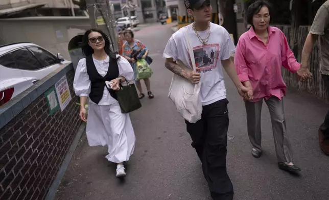 Nicole Motta, left, an adoptee visiting from Los Angeles to search for her birth family, visits the neighborhood where she was born in Bucheon, South Korea, Thursday, May 30, 2024. Her son, Adler, second from left, walks alongside long-time resident An Bok-rye who is helping with her search. (AP Photo/Jae C. Hong)