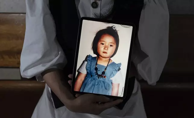 Nicole Motta, an adoptee visiting from Los Angeles, holds a tablet displaying a childhood picture, while traveling to search for her birth family in Yongin, South Korea, Thursday, May 30, 2024. Motta, whose Korean name is Jang Hyeon-jung, visited the site that used to be the orphanage where she stayed until her adoption. (AP Photo/Jae C. Hong)