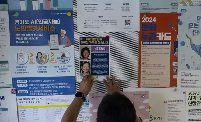 A city worker posts a flier on the crowded bulletin board of a government office in Bucheon, South Korea, Thursday, May 30, 2024. The flier, featuring two photos of Nicole Motta, an adoptee now residing in Los Angeles, taken as a toddler and an adult, was provided by the Global Overseas Adoptees' Link as part of Motta's search for her birth family. (AP Photo/Jae C. Hong)