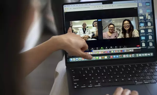 Dee Iraca, at her home in Davidson, N.C., on Friday, April 5, 2024, shows a video of a 2023 video call with her biological father, Park Jong-kyun. She points to fellow adoptee Rebecca Kimmel, left, who sat next to Park in South Korea as Iraca, seen in the window at far right, sits with her twin sister, Becca Webster, back in America. (AP Photo/David Goldman)