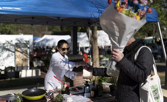 Dee Iraca, left, who was adopted as a baby out of South Korea to a family in the United States, works as chef at a farmer's market Saturday, April 6, 2024, in Davidson, N.C. Iraca and her twin sister are now taking care of their adoptive mother, who has health challenges and it's difficult to find the time and money to visit South Korea. But they want to make the effort to get to know their father. (AP Photo/David Goldman)