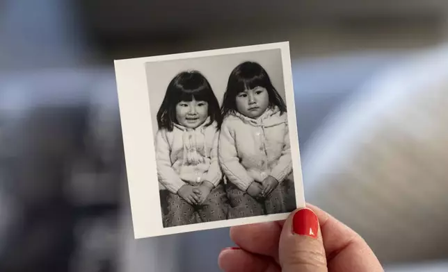 Becca Webster, holds a photo of herself at right, and her twin sister Dee Iraca, who were adopted out of South Korea to a family in the United States, Saturday, April 6, 2024, at Iraca's home in Davidson, N.C. Adopted by the same American family, their files described them as abandoned in front of a hospital. Anytime they thought about searching for their birth parents, they felt overwhelmed. (AP Photo/David Goldman)