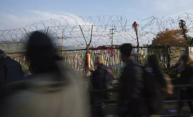 Visitors walk near a wire fence decorated with ribbons written with messages wishing for the reunification of the two Koreas at the Imjingak Pavilion in Paju, South Korea, Thursday, Oct. 31, 2024. (AP Photo/Lee Jin-man)