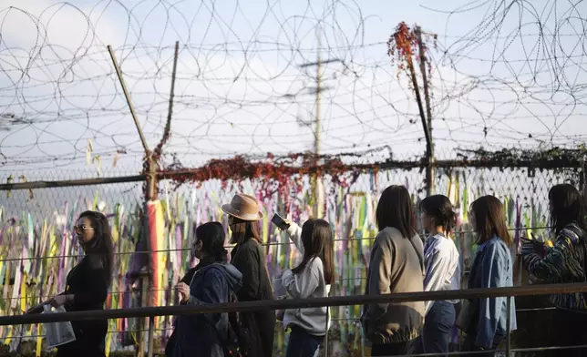 Visitors walk near a wire fence decorated with ribbons written with messages wishing for the reunification of the two Koreas at the Imjingak Pavilion in Paju, South Korea, Thursday, Oct. 31, 2024. (AP Photo/Lee Jin-man)