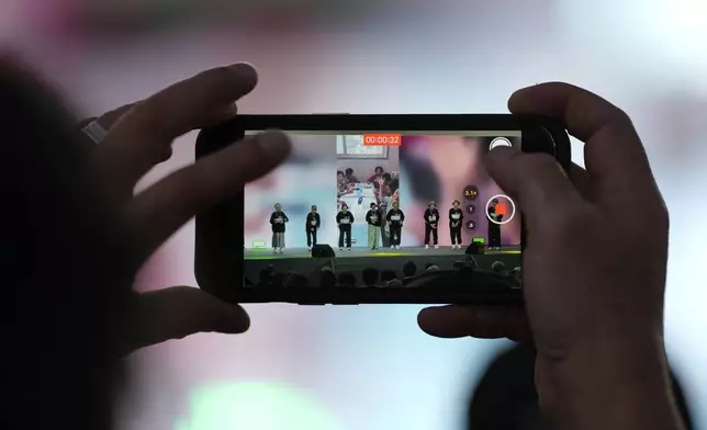 A member of the audience uses a smartphone to film members of Suni and the Seven Princesses performing during the opening ceremony of the Korean alphabet, "Hangeul Week" at Gwanghwamun square in Seoul, South Korea, Friday, Oct. 4, 2024. (AP Photo/Lee Jin-man)