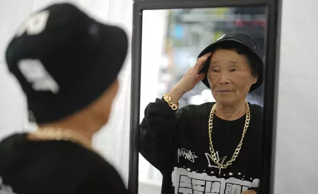 Park Jeom-sun, 82, leader of Suni and the Seven Princesses, adjusts her hat in a mirror during the opening ceremony of the Korean alphabet, "Hangeul Week" at Gwanghwamun square in Seoul, South Korea, Friday, Oct. 4, 2024. (AP Photo/Lee Jin-man)