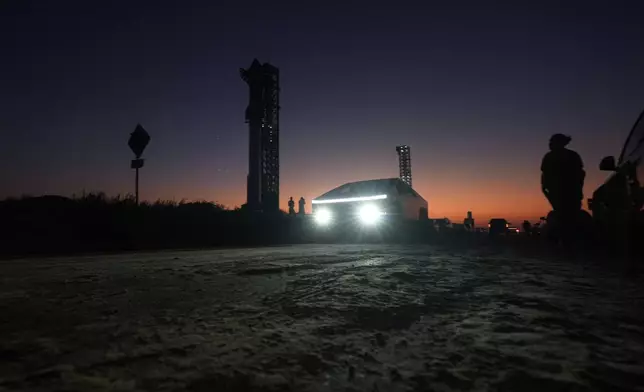 A Tesla Cybertruck passes as the sun sets behind SpaceX's mega rocket Starship, Saturday, Oct. 12, 2024, in Boca Chica, Texas. (AP Photo/Eric Gay)