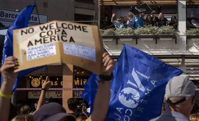 Supporters of America's Cup wave from a restaurant as demonstrators march shouting slogans against the holding of the America's Cup sailing competition, during a protest demanding the right to housing, in Barcelona, Spain, Sunday, Oct. 13, 2024. (AP Photo/Emilio Morenatti)