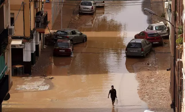 A man carrying water walks through flooded streets in Valencia, Spain, Wednesday, Oct. 30, 2024. (AP Photo/Alberto Saiz)