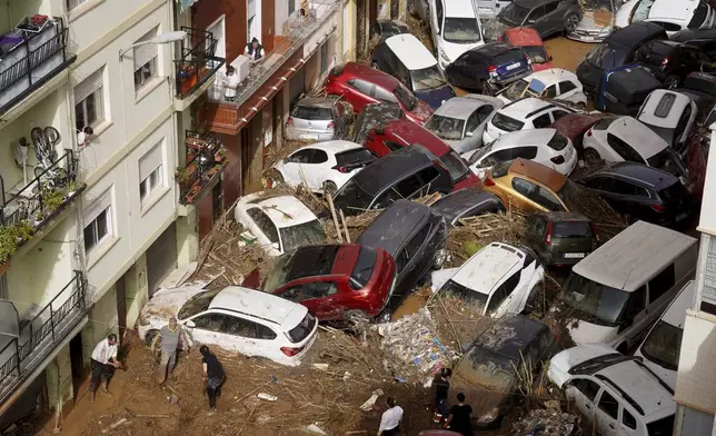 Residents clean the street next to cars piled up after being swept away by floods in Valencia, Spain, Wednesday, Oct. 30, 2024. (AP Photo/Alberto Saiz)