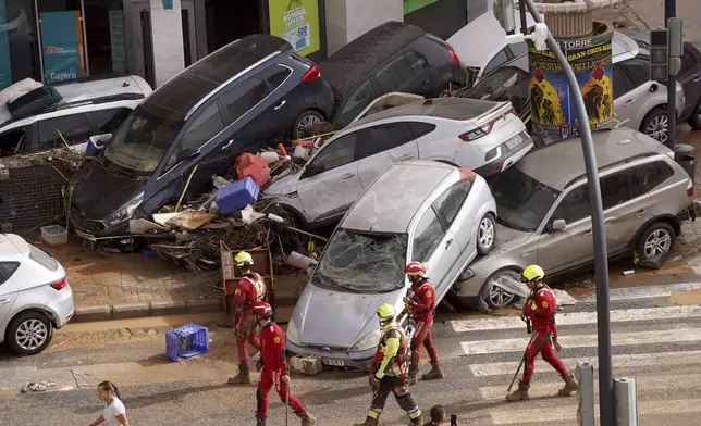 Emergency crew members walk past cars piled up after being swept away by floods in Valencia, Spain, Wednesday, Oct. 30, 2024. (AP Photo/Alberto Saiz)