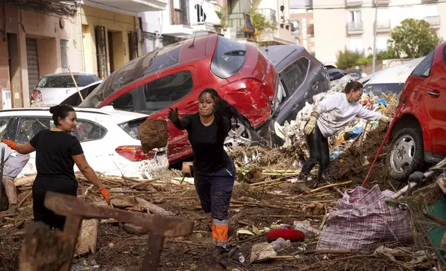 Residents clean the street next to cars piled up after being swept away by floods in Valencia, Spain, Wednesday, Oct. 30, 2024. (AP Photo/Alberto Saiz)