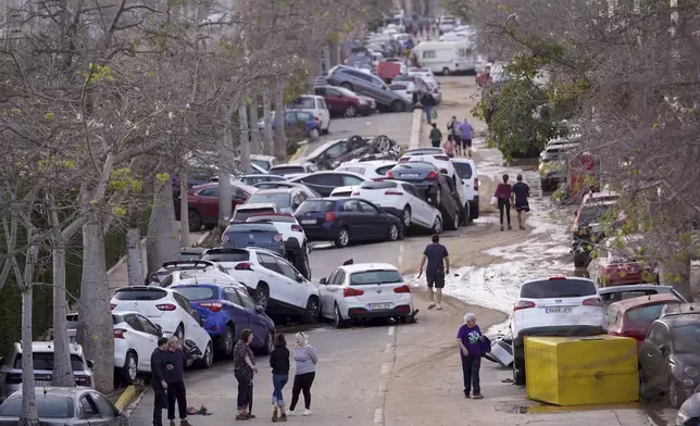 Residents walk next to cars piled up after being swept away by floods in Paiporta, near Valencia, Spain, Wednesday, Oct. 30, 2024. (AP Photo/Alberto Saiz)