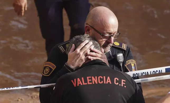 Members of the local police react to the news of one of their colleagues who died in the floods in Valencia, Spain, Thursday, Oct. 31, 2024. (AP Photo/Alberto Saiz)