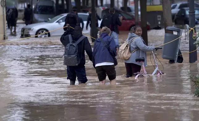 People walk through flooded streets in Valencia, Wednesday, Oct. 30, 2024. (AP Photo/Alberto Saiz)