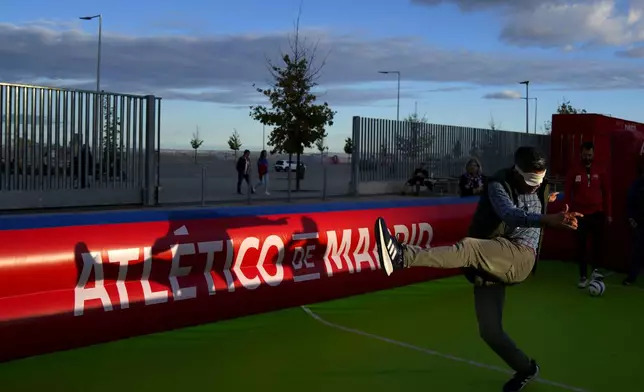 A fan tries to kick a ball with a blindfold on before going to see the Champions League opening phase soccer match between Atletico Madrid and Lille at the Metropolitano stadium in Madrid, Spain, Wednesday, Oct. 23, 2024. (AP Photo/Manu Fernandez)