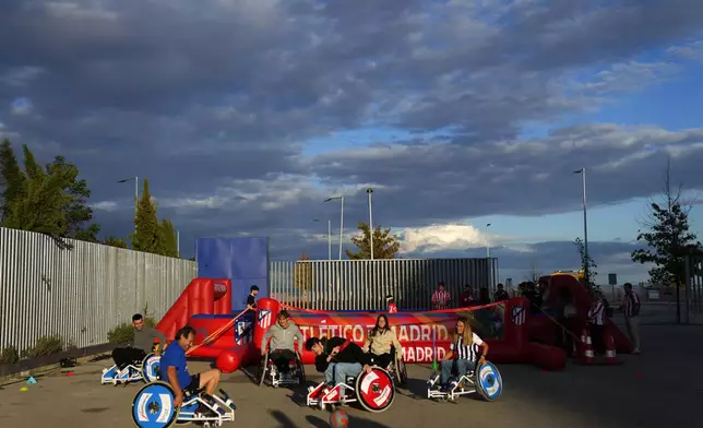 Fans try to play soccer in wheelchairs before going to see the Champions League opening phase soccer match between Atletico Madrid and Lille at the Metropolitano stadium in Madrid, Spain, Wednesday, Oct. 23, 2024. (AP Photo/Manu Fernandez)