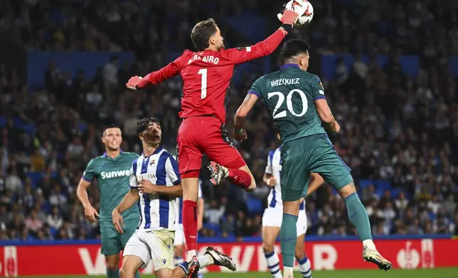 Real Sociedad's goalkeeper Alex Remiro reaches for the ball over Anderlecht's Luis Vazquez to make a save during the Europa League opening phase soccer match between Real Sociedad and Anderlecht at the Reale Arena in San Sebastian, Spain, Thursday, Oct. 3, 2024. (AP Photo/Miguel Oses)