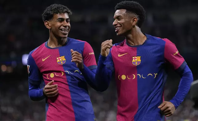Barcelona's Lamine Yamal, left, celebrates with Barcelona's Alejandro Balde after scoring his side's third goal during a Spanish La Liga soccer match between Real Madrid and Barcelona at the Santiago Bernabeu stadium in Madrid, Spain, Saturday, Oct. 26, 2024. (AP Photo/Manu Fernandez)