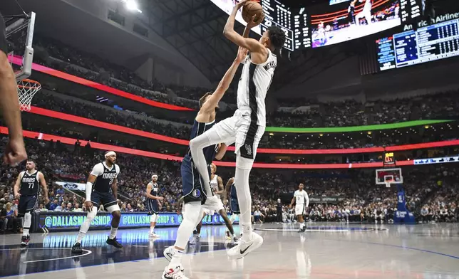 San Antonio Spurs center Victor Wembanyama, center right, is defended by Dallas Mavericks forward Maxi Kleber, center left, as he shoots a jump shot during the first half of an NBA basketball game, Thursday, Oct. 24, 2024, in Dallas, Texas. (AP Photo/Albert Pena)