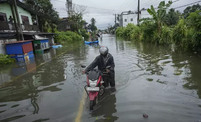 A man pushes his motorbike along a flooded road in Colombo, Sri Lanka, Monday, Oct. 14, 2024. (AP Photo/Eranga Jayawardena)