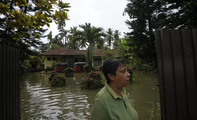 A woman stands outside her submerged house due to floods in Colombo, Sri Lanka, Sunday, Oct. 13, 2024. (AP Photo/Eranga Jayawardena)